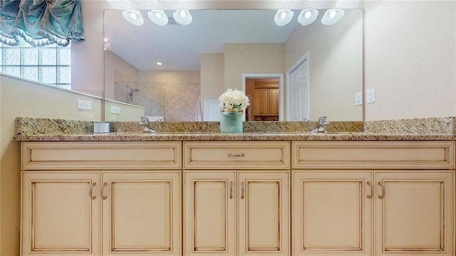 full bathroom with double vanity, tiled shower, and a sink