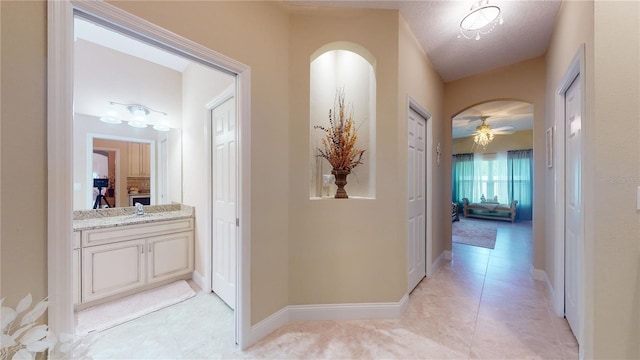 corridor featuring arched walkways, light tile patterned floors, a textured ceiling, a sink, and baseboards