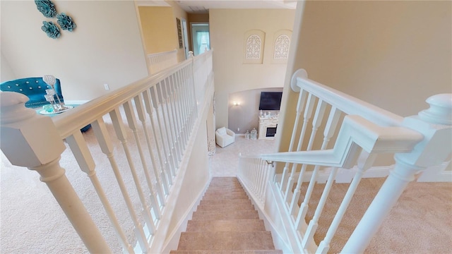 stairway featuring a towering ceiling, a fireplace, and carpet flooring