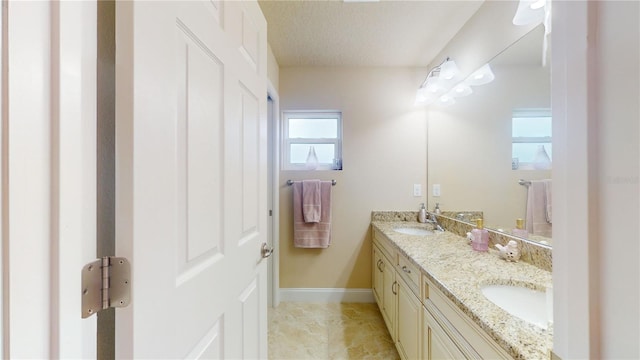 full bath featuring a sink, a textured ceiling, baseboards, and double vanity