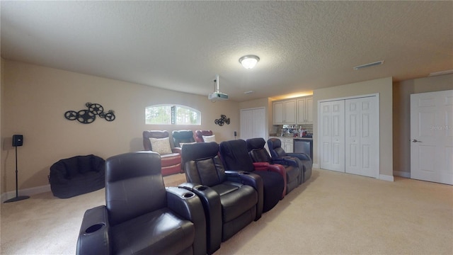 cinema room featuring a textured ceiling, baseboards, visible vents, and light colored carpet