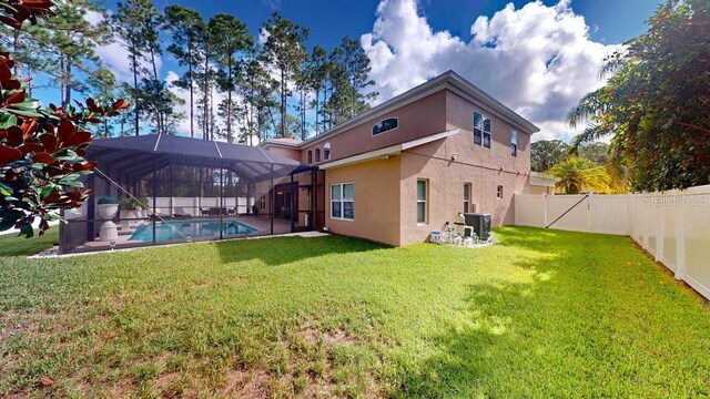 rear view of property featuring glass enclosure, central AC unit, a lawn, and a fenced in pool