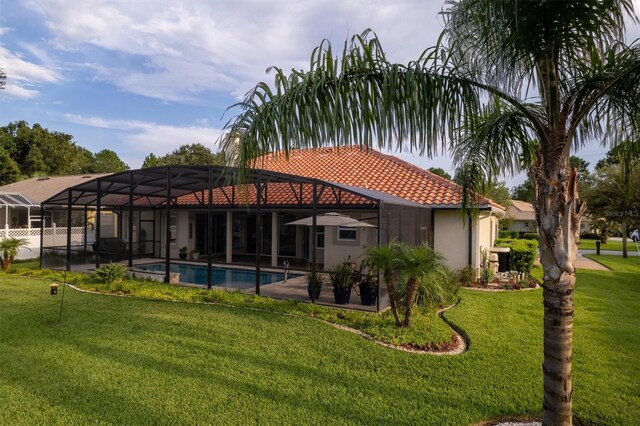 rear view of house featuring glass enclosure, a lawn, and a patio