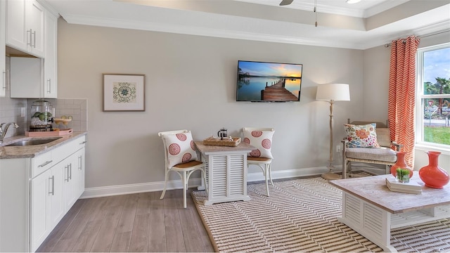 living area with ornamental molding, light wood-type flooring, and baseboards