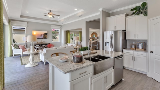 kitchen with a tray ceiling, stainless steel appliances, a center island with sink, and light hardwood / wood-style floors