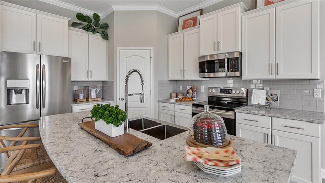 kitchen featuring a breakfast bar, backsplash, appliances with stainless steel finishes, white cabinetry, and crown molding