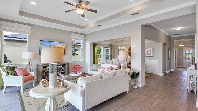 living room featuring ceiling fan with notable chandelier, crown molding, a tray ceiling, and wood-type flooring