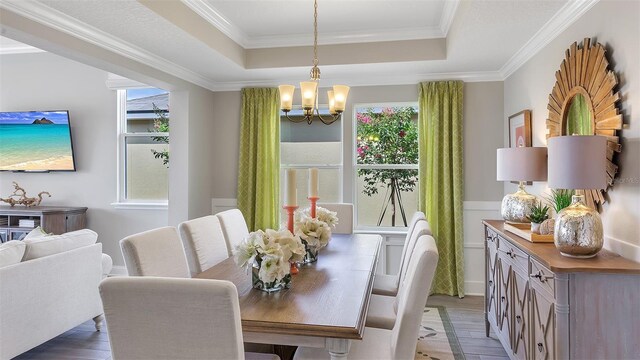 dining room with hardwood / wood-style flooring, a raised ceiling, a chandelier, and ornamental molding