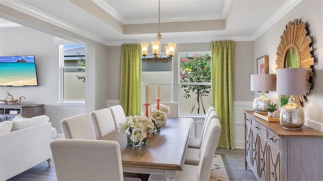 dining space with a chandelier, a raised ceiling, ornamental molding, and wood finished floors