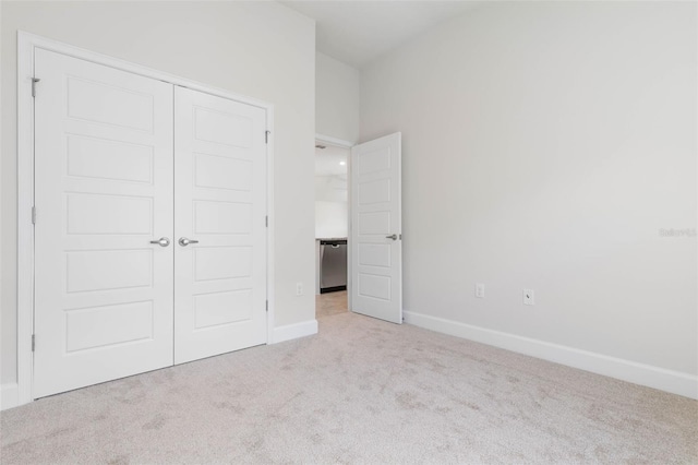 unfurnished bedroom with a closet, light colored carpet, and baseboards