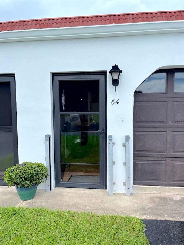 property entrance featuring a garage, stucco siding, and a tiled roof