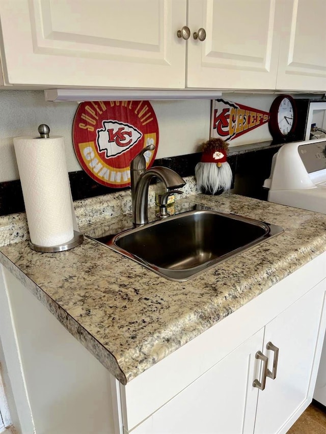 interior details featuring light stone counters, a sink, white cabinetry, and wet bar