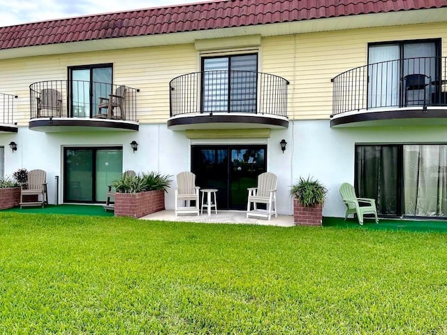 rear view of property featuring a lawn, a patio, a balcony, a tiled roof, and stucco siding