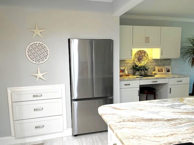 kitchen with decorative backsplash, ornamental molding, light stone counters, freestanding refrigerator, and white cabinetry