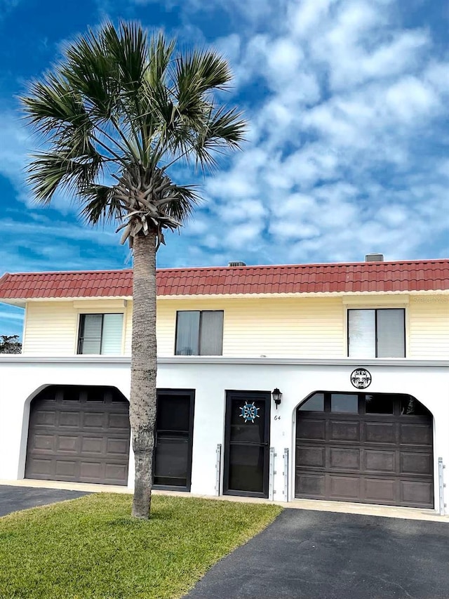 view of front of house with a garage, driveway, a tiled roof, and stucco siding