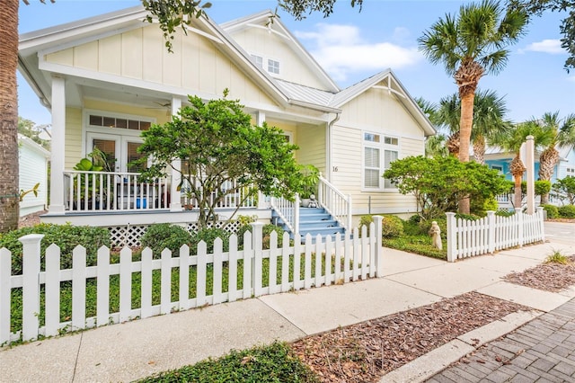 view of front facade featuring board and batten siding, covered porch, metal roof, and a fenced front yard