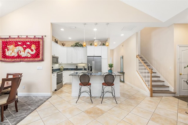 kitchen with light tile patterned floors, stainless steel appliances, a kitchen island with sink, vaulted ceiling, and white cabinetry