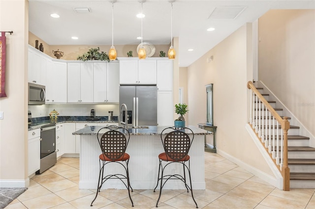 kitchen featuring appliances with stainless steel finishes, an island with sink, a breakfast bar, and white cabinets