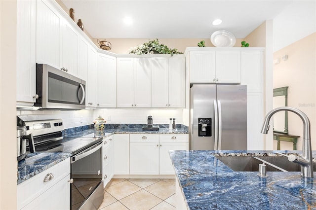 kitchen with stainless steel appliances, tasteful backsplash, light tile patterned flooring, a sink, and white cabinetry