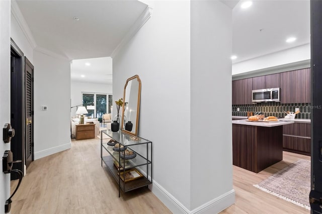 hallway featuring baseboards, light wood-type flooring, and crown molding