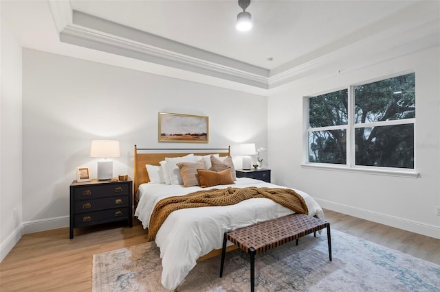 bedroom with crown molding, a tray ceiling, light wood-type flooring, and baseboards