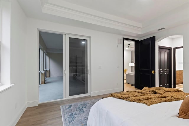 bedroom with a raised ceiling, connected bathroom, a closet, and wood-type flooring