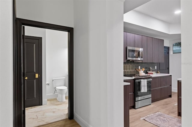 kitchen with decorative backsplash, light wood-style flooring, modern cabinets, appliances with stainless steel finishes, and light countertops