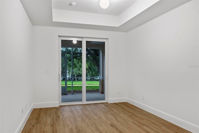 empty room featuring a tray ceiling, baseboards, and wood finished floors