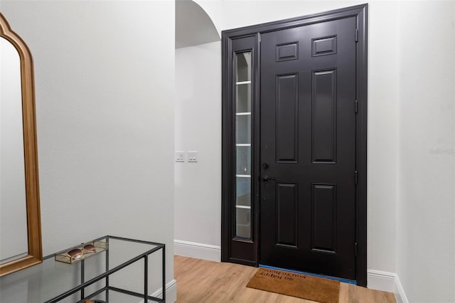 entryway featuring arched walkways, light wood-style flooring, and baseboards