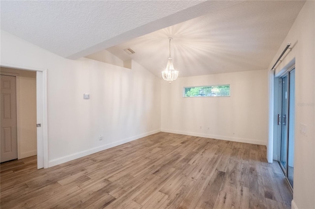 spare room featuring vaulted ceiling, an inviting chandelier, a textured ceiling, and light hardwood / wood-style flooring