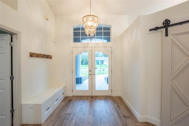 interior space featuring a barn door, light wood-type flooring, an inviting chandelier, and french doors