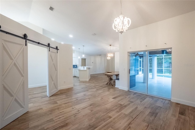 unfurnished living room featuring light wood-type flooring, a notable chandelier, high vaulted ceiling, and a barn door