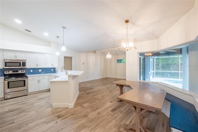 kitchen with hanging light fixtures, appliances with stainless steel finishes, lofted ceiling, white cabinets, and light hardwood / wood-style floors