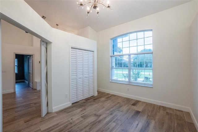 unfurnished bedroom featuring a chandelier, hardwood / wood-style floors, and a closet