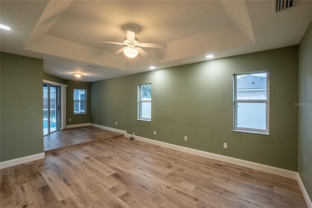 empty room featuring light wood-type flooring, ceiling fan, and a raised ceiling