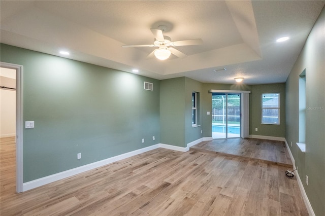 unfurnished room featuring a raised ceiling, ceiling fan, and light hardwood / wood-style floors