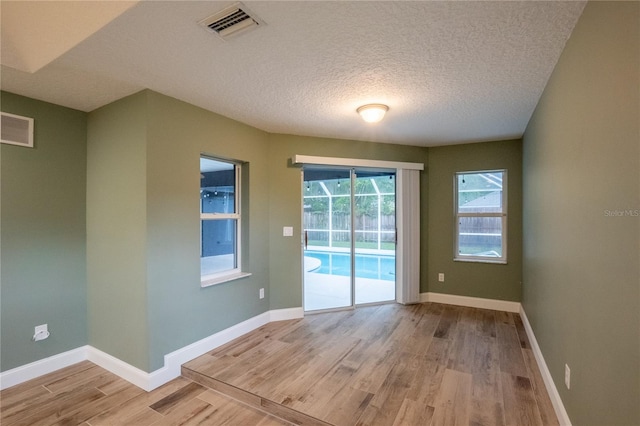 unfurnished room with light wood-type flooring and a textured ceiling