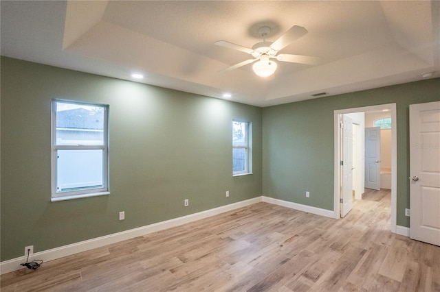 unfurnished bedroom with multiple windows, ceiling fan, a tray ceiling, and light hardwood / wood-style flooring