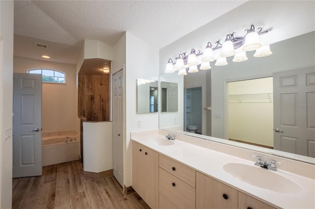 bathroom featuring toilet, a bathing tub, wood-type flooring, vanity, and a textured ceiling