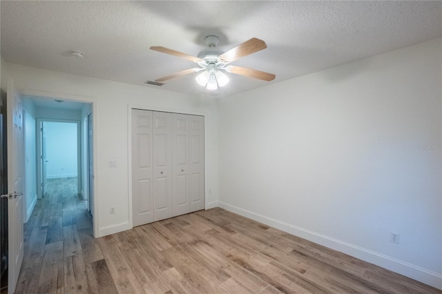 unfurnished bedroom with a textured ceiling, ceiling fan, a closet, and light wood-type flooring