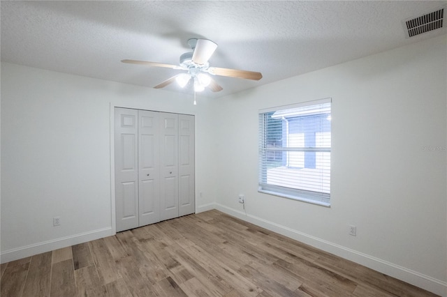 unfurnished bedroom featuring light wood-type flooring, a textured ceiling, ceiling fan, and a closet