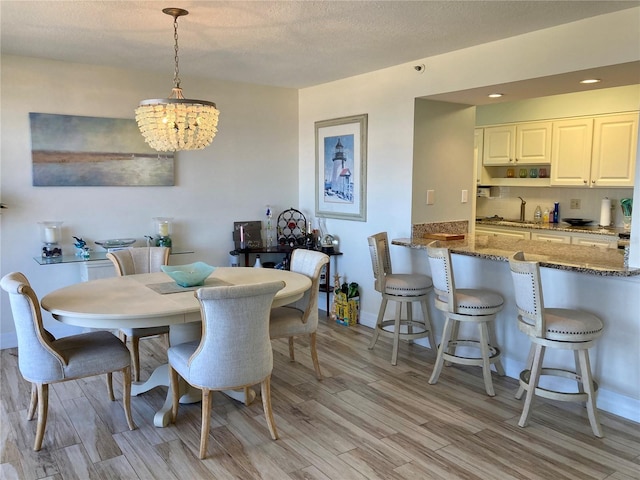 dining room featuring sink, an inviting chandelier, a textured ceiling, and light hardwood / wood-style flooring