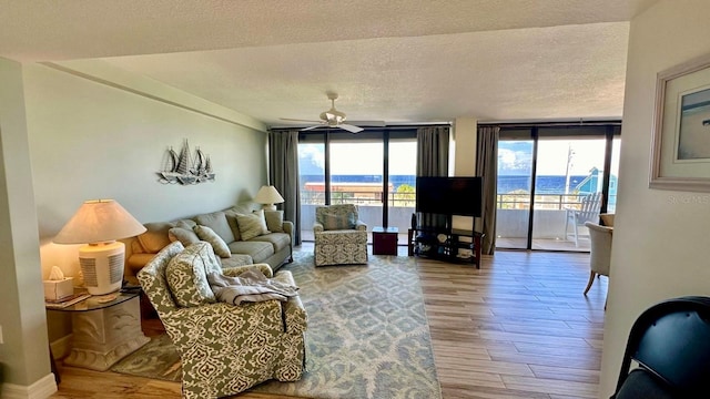 living room featuring plenty of natural light, ceiling fan, a wall of windows, and light hardwood / wood-style floors