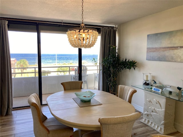 dining space featuring a water view, hardwood / wood-style flooring, a notable chandelier, and a textured ceiling