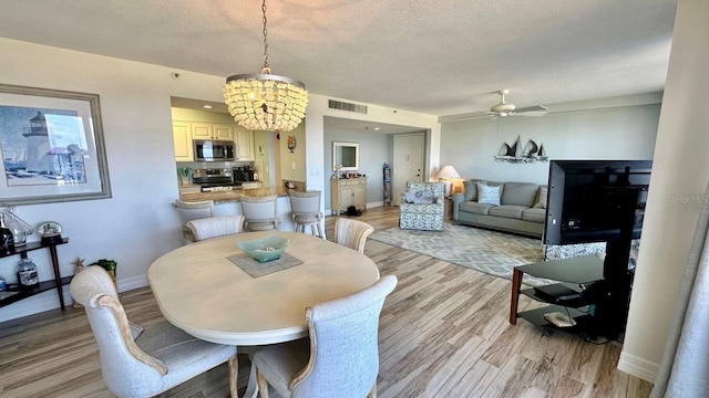 dining room featuring ceiling fan with notable chandelier, a textured ceiling, and light hardwood / wood-style flooring