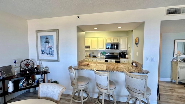 kitchen featuring dark stone countertops, light wood-type flooring, stainless steel appliances, kitchen peninsula, and a textured ceiling