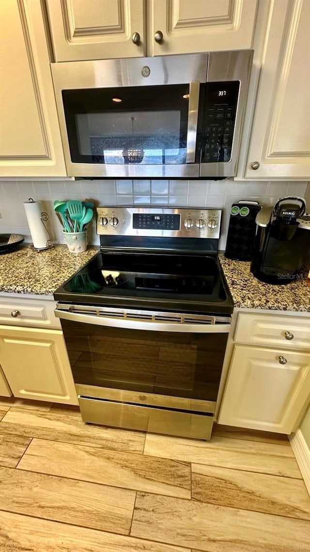 kitchen with light hardwood / wood-style flooring, light stone counters, appliances with stainless steel finishes, and tasteful backsplash