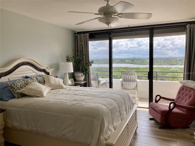 bedroom with hardwood / wood-style flooring, a water view, access to exterior, ceiling fan, and a textured ceiling