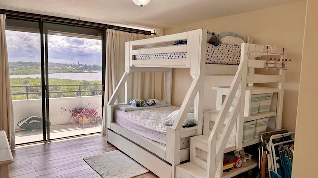 bedroom with a textured ceiling, access to exterior, wood-type flooring, and a water view