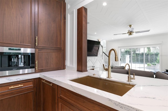 kitchen featuring sink, vaulted ceiling, light stone countertops, ceiling fan, and stainless steel oven